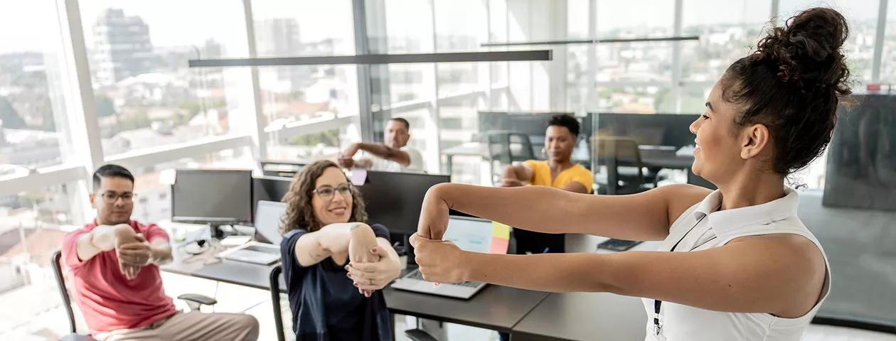 Quatro trabalhadores fazem ginástica laboral no escritório com uma professora 
