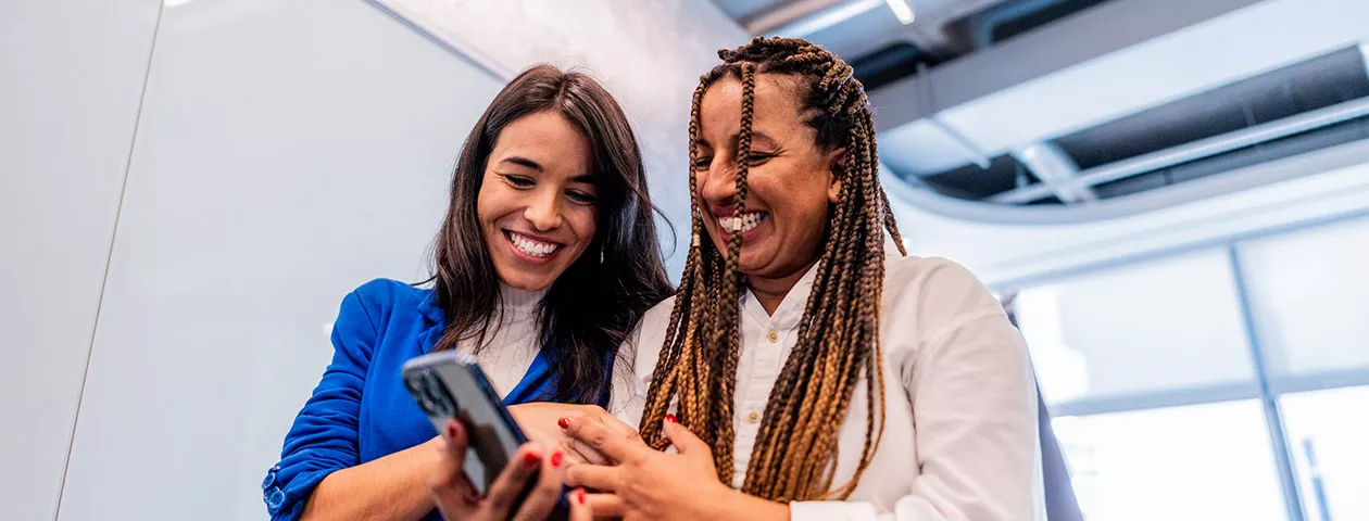 Duas amigas de trabalho conferem no celular os benefícios para funcionários que recebem da empresa 