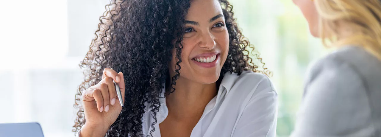 mulher sorrindo enquanto explica algo para outra. 