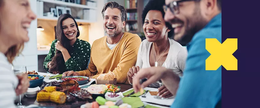 A imagem mostra pessoas conversando com comidas na mesa em que elas estão