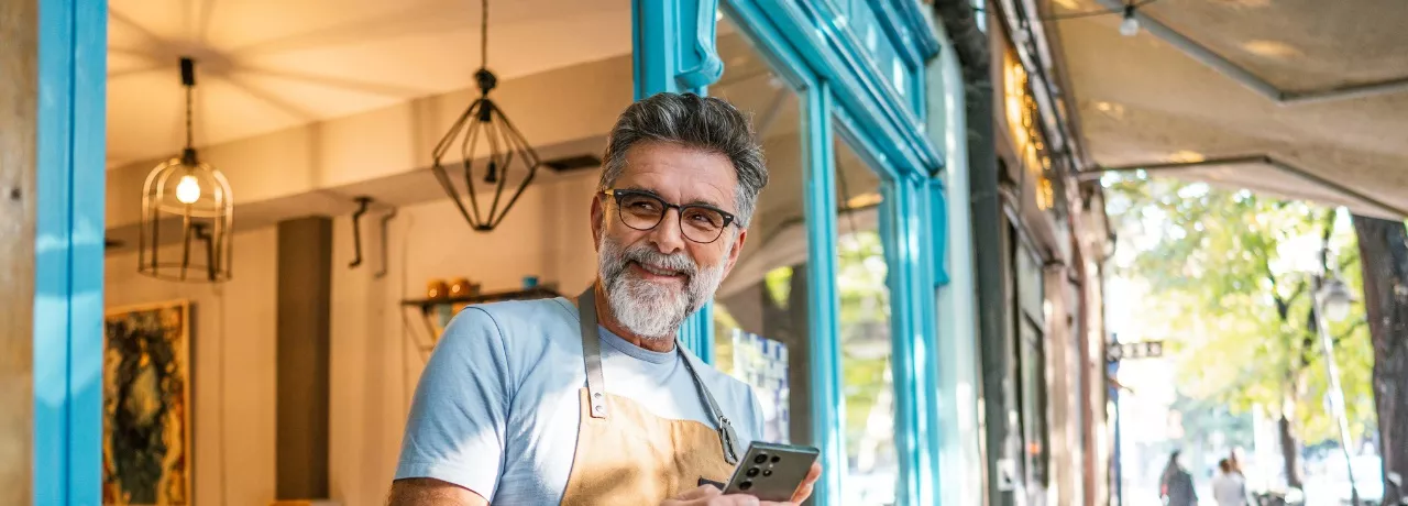 A imagem mostra um homem usando avental na frente de um estabelecimento 