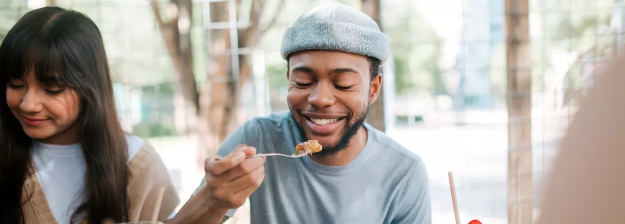 A imagem mostra um rapaz e uma mulher se alimentando ao ar livre 