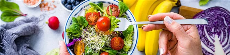 Imagem mostra uma salada com tomates e frutas ao fundo 