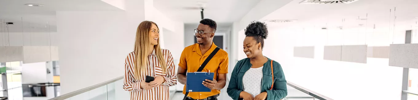 três pessoas conversando e rindo em corredor.