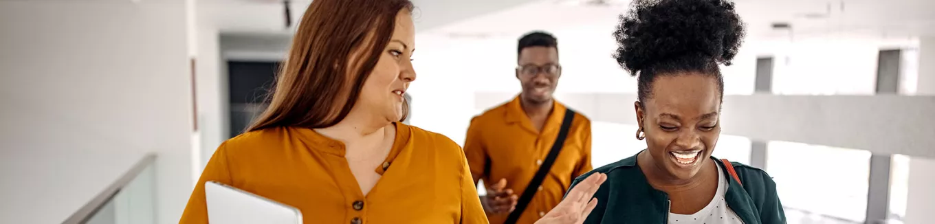 três pessoas conversando e rindo em corredor. 