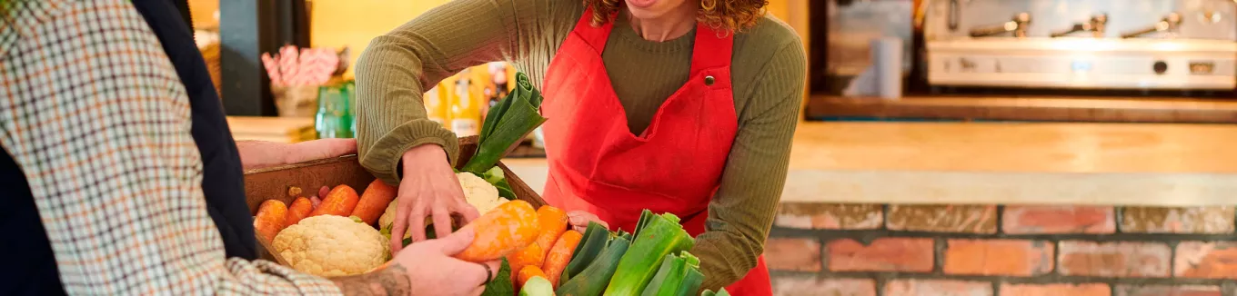 foto mostra duas pessoas mexendo em uma cesta de legumes frescos 