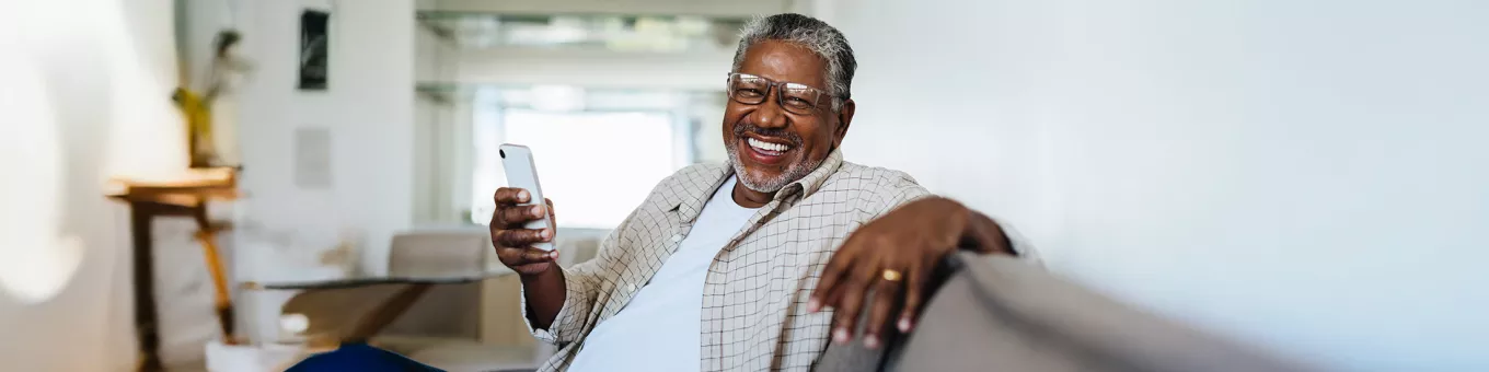 Foto mostra trabalhador na sala de casa com um celular na mão 