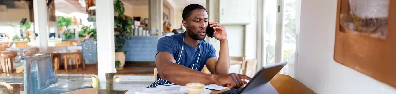 dono de empresa falando no telefone enquanto usa notebook. 
