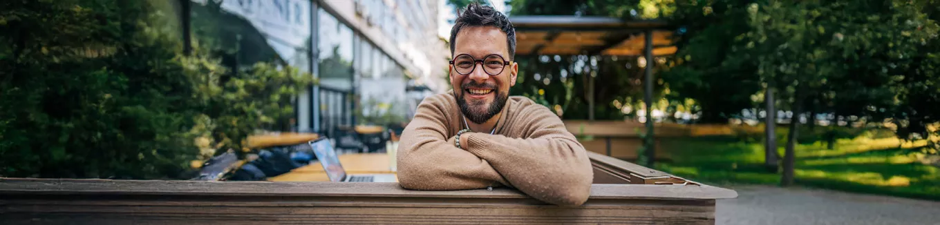 Homem sorrindo de braços cruzados no ambiente corporativo 