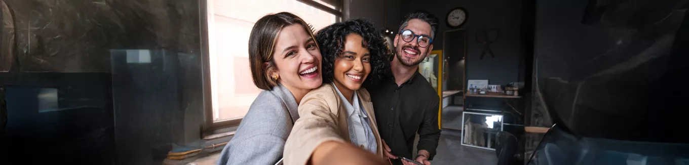 Foto mostra três colegas de trabalho tirando uma selfie no escritório 