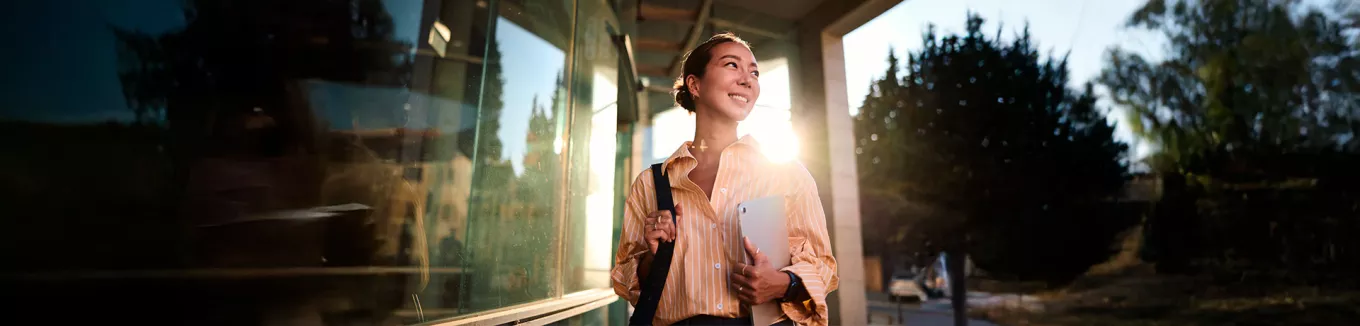 Foto de uma jovem profissional na área externa da empresa em que trabalha 