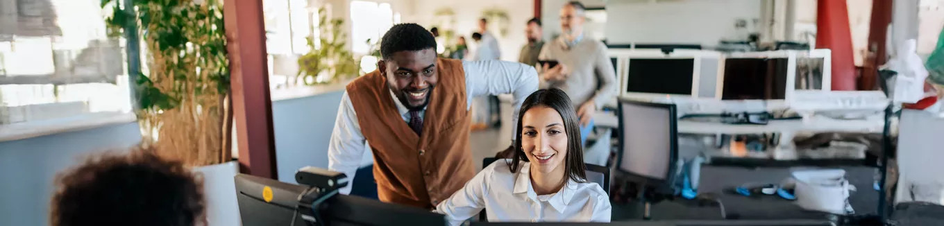 um homem e uma mulher sorrindo olhando para computador em escritório. 