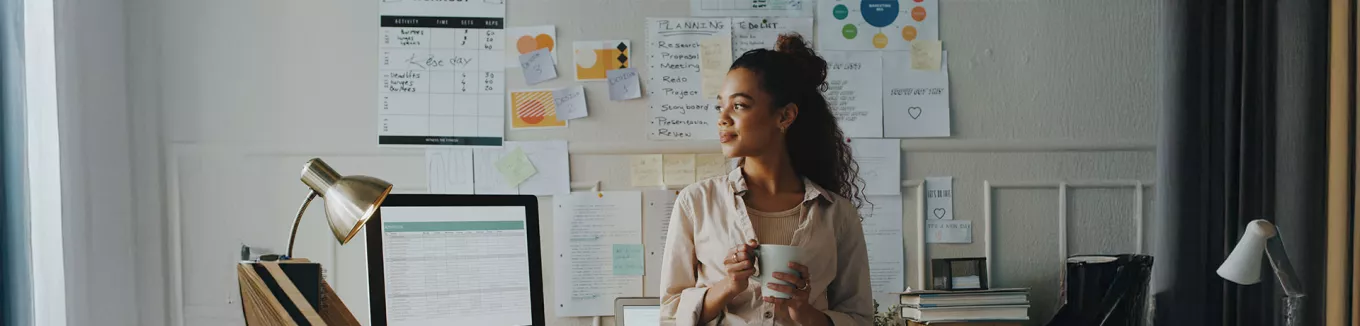 mulher segurando xícara de café em frente a uma série de papéis com planejamento estratégico. 