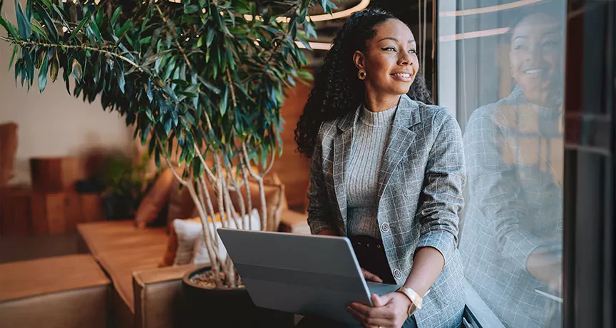 mulher empreendedora olhando pela janela sorrindo com notebook no colo. 