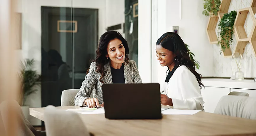 duas mulheres conversando enquanto olham algo em notebook. 