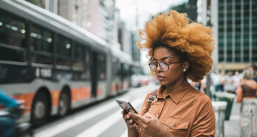 mulher usando o celular enquanto onibus do sistema de transporte de são paulo passa ao lado.
