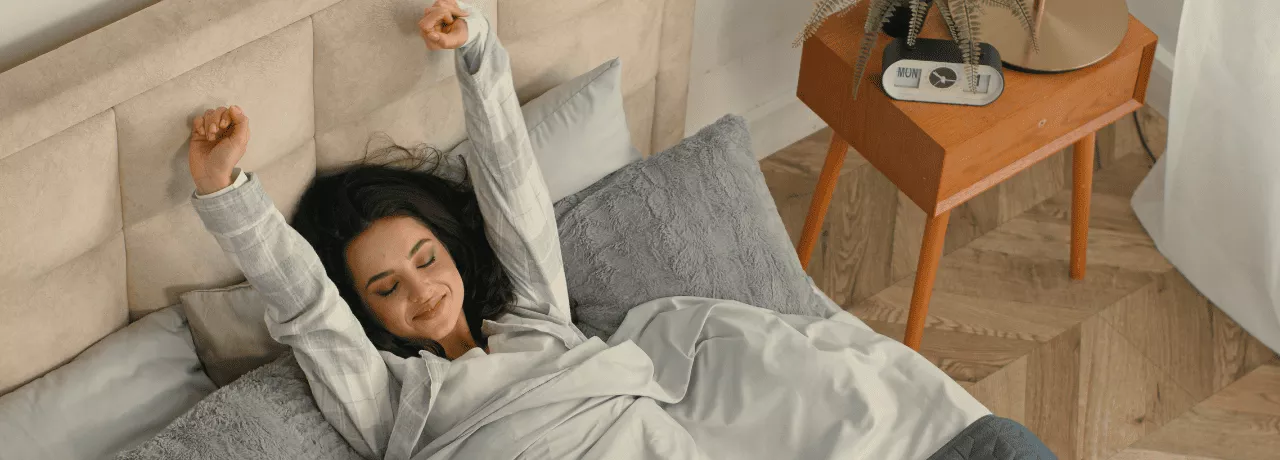 A imagem mostra uma mulher em uma cama, se espreguiçando ao acordar