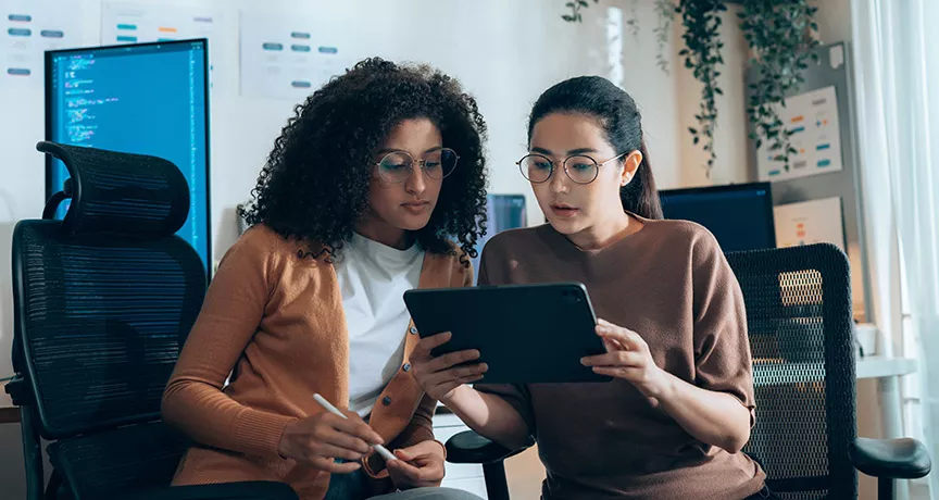 duas mulheres discutindo sobre algo enquanto olham tablet. 