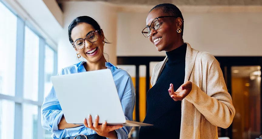 duas mulheres conversando animadamente enquanto veem algo em computador.