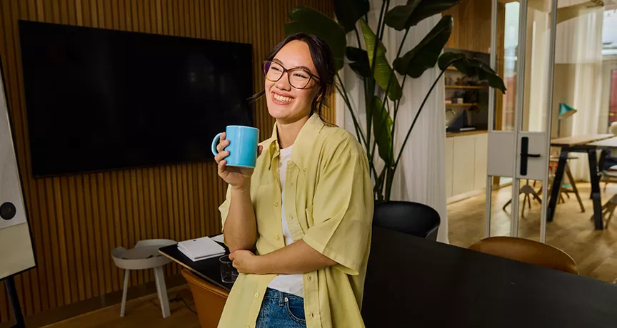 mulher sorrindo enquanto bebe algo em caneca.