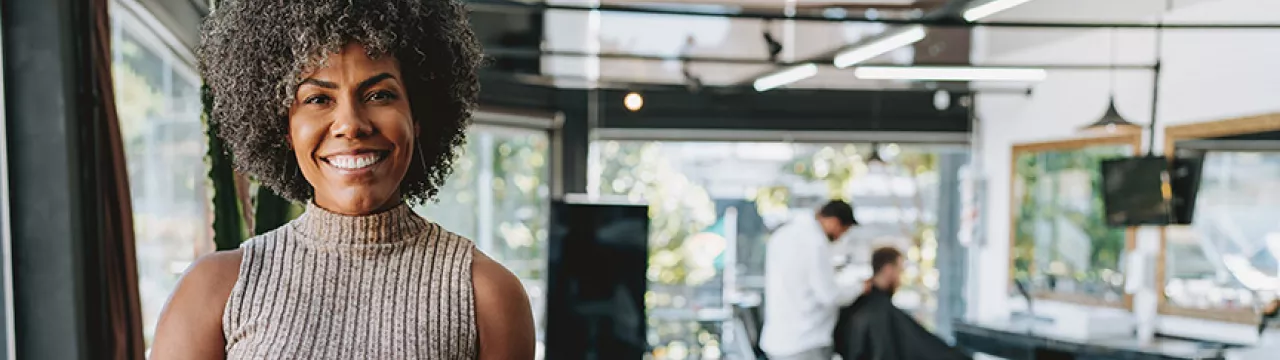 Dona de salão de beleza sorri para a câmera, mostrando seu estabelecimento