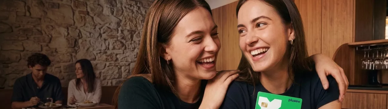 A imagem mostra duas pessoas sorrindo e segurando um cartão Pluxee