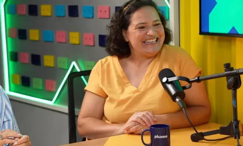 Pessoa sentada em estúdio de podcast falando ao microfone sobre uma mesa