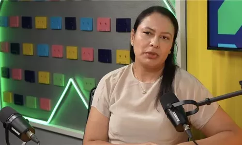 Pessoa sentada em estúdio de podcast falando ao microfone sobre uma mesa