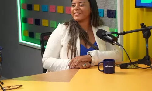 Pessoa sentada em estúdio de podcast falando ao microfone sobre uma mesa