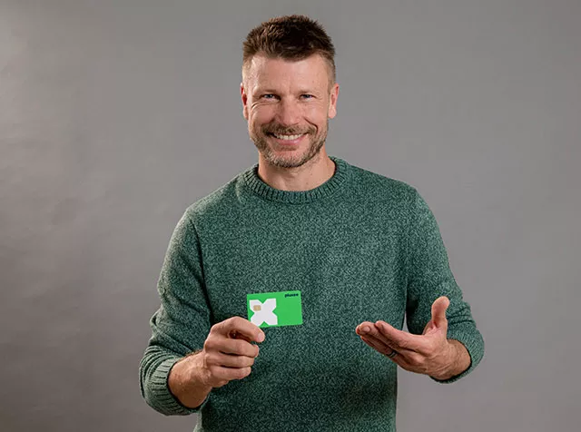 Rodrigo Hilbert sorri com o cartão Pluxee na mão