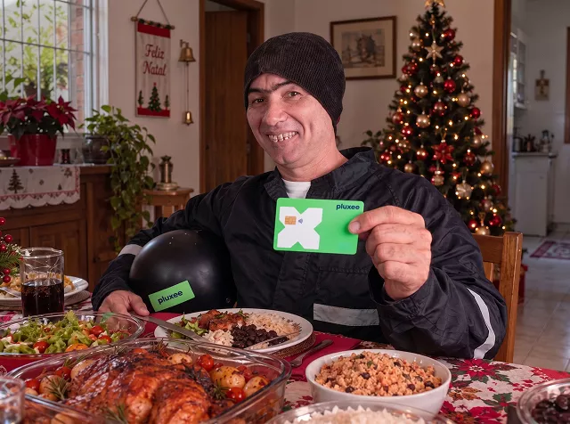 Foto de uma pessoa em sua ceia de Natal com o cartão Pluxee na mão