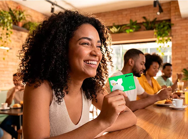 Mulher mostra o cartão Pluxee Multibenefícios Elo no restaurante