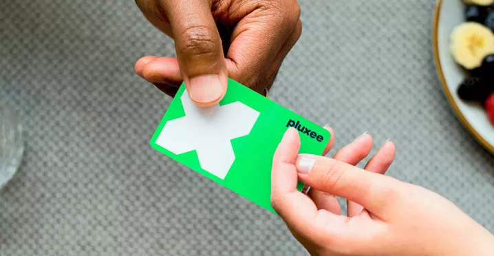 Mulher usa o cartão de benefício Pluxee para pagar uma conta. Nossos cartões são feitos com plástico reciclável!