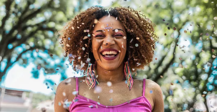 Foto mostra mulher sorridente pulando Carnaval numa praça
