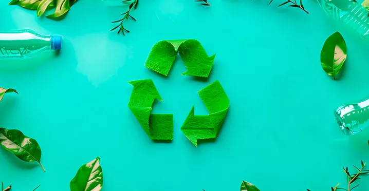 Imagem mostra um símbolo verde de reciclagem num fundo verde, com algumas garrafas de plástico vazias ao redor