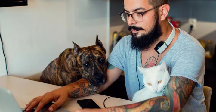 Homem trabalha de casa na companhia de seu cachorro e de seu gato