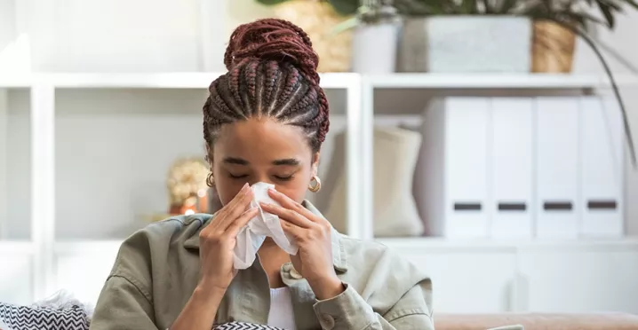 Foto mostra uma mulher assoando o nariz porque está resfriada 