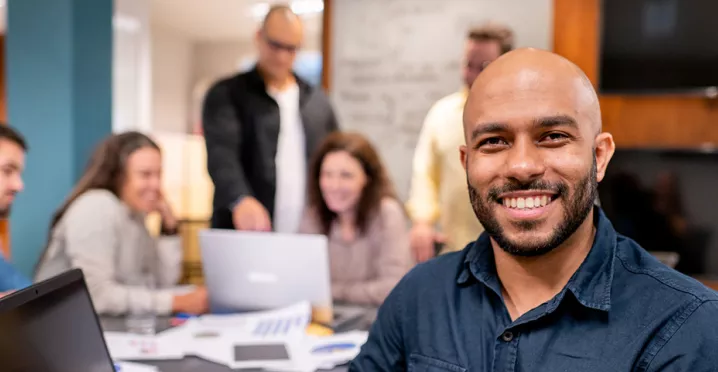 Foto mostra uma equipe de trabalho, com um homem sorrindo em destaque na frente
