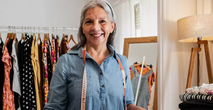 mulher grisalha dona de uma loja de roupas sorrindo para a câmera.
