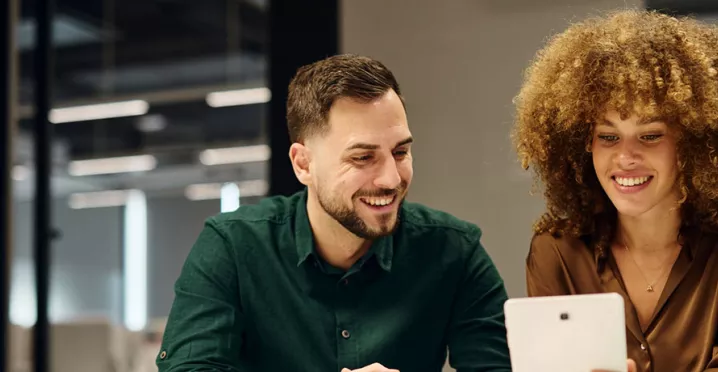 um homem e uma mulher sorrindo olhando para tablet.