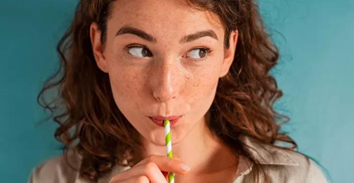 Foto mostra uma mulher tomando uma bebida de canudinho
