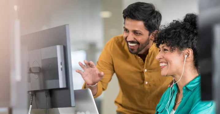 duas pessoas conversando e sorrindo em frente a um computador.