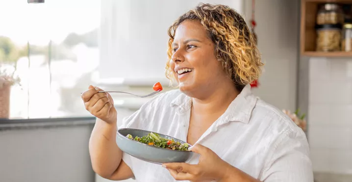 mulher comendo salada sorrindo.
