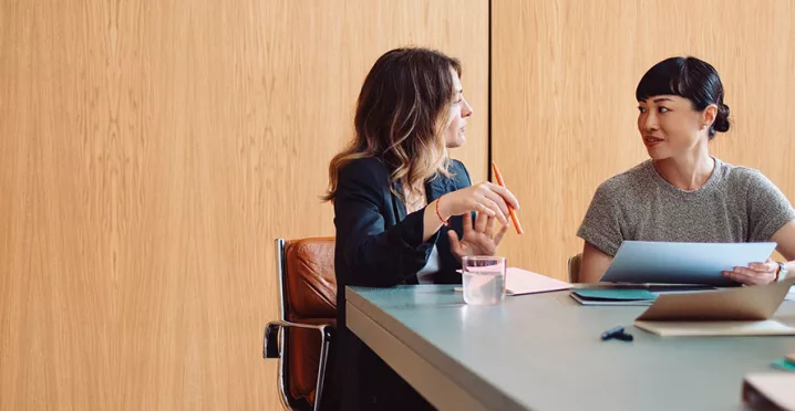 duas mulheres conversando em uma sala de reunião enquanto anotam algo.