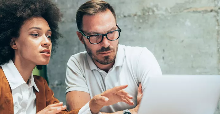 duas pessoas conversando sobre algo enquanto apontam para a tela do notebook.