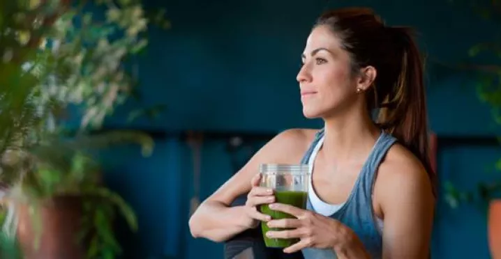 Imagem mostra uma mulher branca tomando um suco verde 
