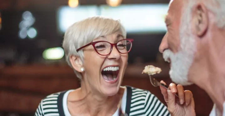 A imagem mostra um casal com cabelos grisalhos se alimentando em um restaurante