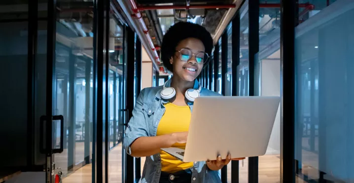 mulher sorrindo enquanto segura computador e caminha em um corredor de escritório.