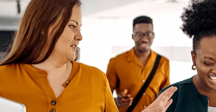 três pessoas conversando e rindo em corredor.