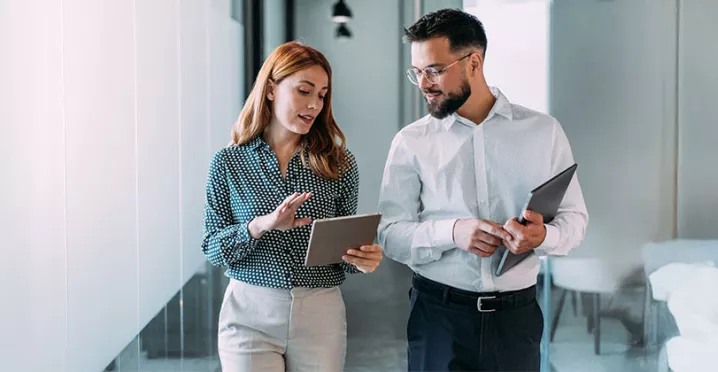 duas pessoas conversando enquanto olham dado em tablet dentro de uma empresa.